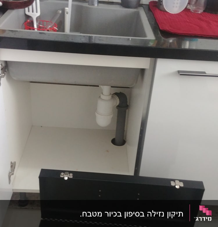 ארגז כלים פתוח ליד כיור מטבח עם צנרת גלויה